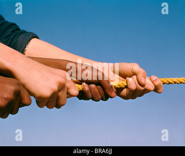 1960s CAUCASIAN AND AFRICAN AMERICAN HANDS PULLING ON ROPE Stock Photo