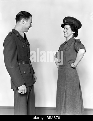 1940s COUPLE MAN IN UNIFORM WOMAN SMILING WEARING HIS HAT HANDS ON HIPS Stock Photo