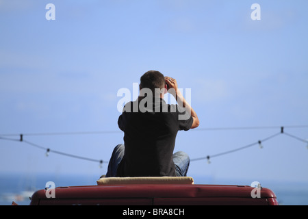 A man watches Eastbourne Air Show from the roof of a van. Stock Photo