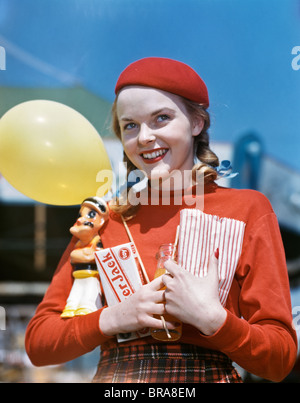 1940s 1950s SMILING TEEN GIRL HOLDING POPEYE AMUSEMENT PARK PRIZE CRACKER JACK BOX YELLOW BALLOON WEARING RED TAM Stock Photo