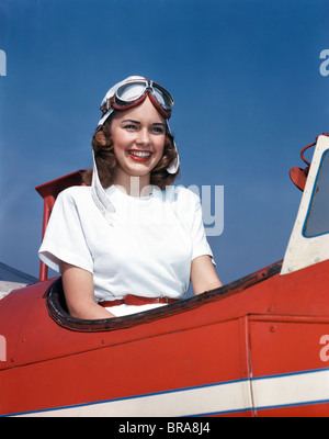 1940s 1950s SMILING WOMAN WEARING PILOTS HELMET GOGGLES SITTING IN AIRPLANE OPEN COCKPIT Stock Photo