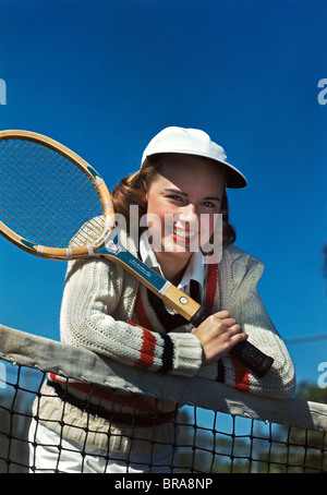 1940s 1950s SMILING TEEN GIRL HOLDING TENNIS RACQUET LEANING OVER TENNIS NET Stock Photo