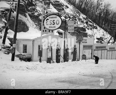 1940s SERVICE STATION IN MOUNTAINS IN WINTER SEVERAL GAS PUMPS GARAGES & OIL & GAS SIGNS Stock Photo