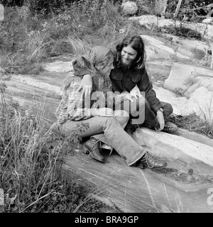 1960s 1970s ROMANTIC YOUNG HIPPIE COUPLE SITTING OUTDOORS Stock Photo