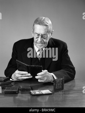 1940s ELDERLY MAN WEARING GLASSES SITTING AT TABLE LOOKING AT DAGUERREOTYPE PHOTOGRAPHS Stock Photo
