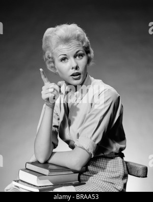 1950s 1960s BLOND WOMAN STACK OF BOOKS IN HER LAP SHAKING FINGER POINTING Stock Photo