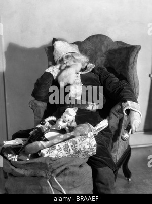 1920s 1930s SANTA CLAUS ASLEEP IN ARMCHAIR WITH BAG SACK OF TOYS Stock Photo