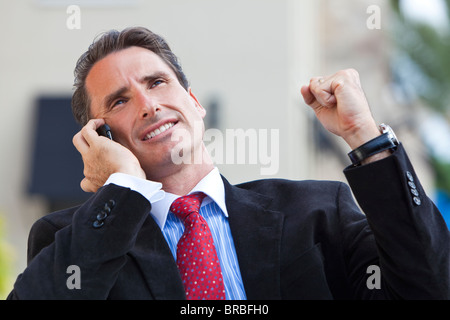 A businessman with clenched fist pump celebrating success while talking on his mobile cell phone Stock Photo