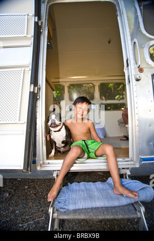 boy sitting in door of camper with dog Stock Photo