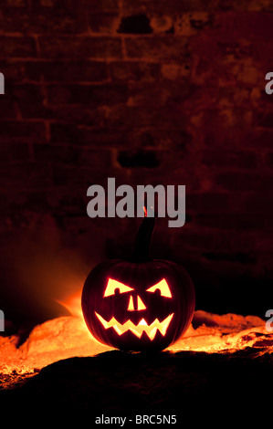 Halloween pumpkin, Jack o lantern, face and fire against a dark brick wall Stock Photo
