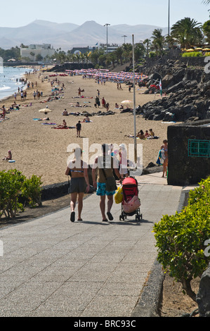 dh beach PUERTO DEL CARMEN LANZAROTE Tourist couple pushchair walking down to beach young holidays family holiday Stock Photo