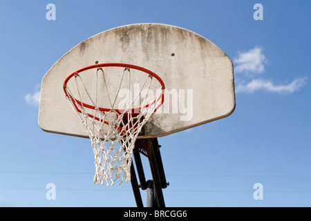 A weathered fiberglass basketball backboard, with attached rim and net against a blue sky. Focus is on the rim and net. Stock Photo