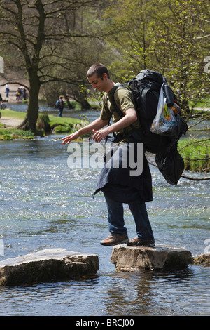 Walker with heavy rucksack crossing the Dovedale Stepping Stones, Peak District, Derbyshire Stock Photo