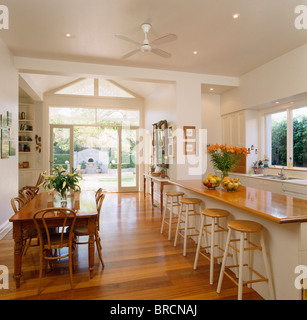 Old pine table and bentwood chairs in dining area of large open-plan kitchen with wooden stools on breakfast bar on long island Stock Photo