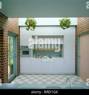 Blue+white tiled floor and brick walls in modern kitchen with white fitted units on one wall Stock Photo