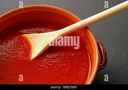 Terracotta pot and wooden spoon with tomato sauce Stock Photo