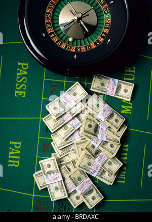 Wads of 100 American Dollars notes and roulette wheel on casino green baize Stock Photo