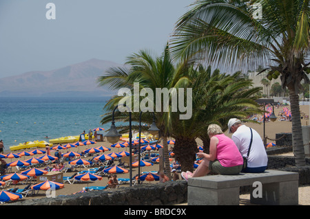 A middle aged couple sitting by the beach at Puerto Del Carmen, Lanzarote, Canary Islands Stock Photo