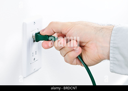 Hand inserting green electrical plug into outlet