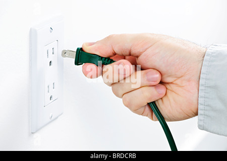 Hand inserting green electrical plug into outlet Stock Photo