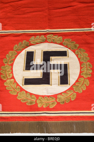 Adolf Hitler - a tapestry, from the Brown House in Munich Heavy version made of red fabric, in the centre a gold-bordered, upright black swastika in a white disc surrounded by gold oak leaf embroidery. Rectangular, black-white-golden border. Fringe trim on the lower edge. The upper edge with a broad hem, inside a sleeve for the wall hanging rod. Small damages, the red silk backing with repairs. Size 220 x 190 cm. From a series of tapestries from Adolf Hitler's personal meeting room in the party building complex "Braunes Haus" in Munich, Briennerstr. 45. Cf. Her, Stock Photo