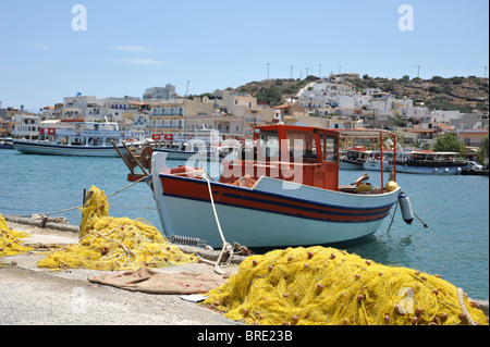 Yellow fishing nets and fishing boat moored in the harbour in Elounda, Crete, Greece Stock Photo