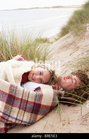 Teenage Couple Sitting In Sand Dunes Wrapped In Blanket Stock Photo