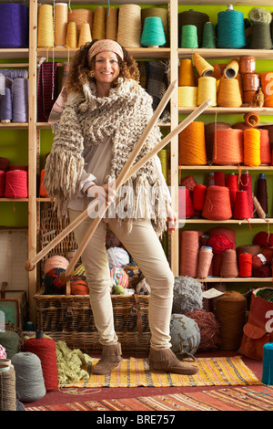 Woman Wearing Knitted Scarf Standing In Front Of Yarn Display Holding Giant Needles Stock Photo