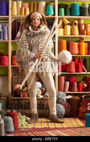 Woman Wearing Knitted Scarf Standing In Front Of Yarn Display Holding Giant Needles Stock Photo
