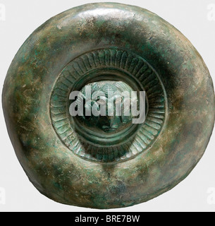 A decorative Etruscan shield, circa 500 B.C. Bronze. The separately made central medallion displays a ram's head in high relief with remnants of white eye inlays (colour paint?), surrounded by an ornamental ring bearing a tongue pattern, and a broad, strongly rounded protuding rim. Diameter 28.5 cm. Broken into small pieces, glued together and stabilised with fiberglass. Restorations at various places. Axel Guttmann Collection (R 203/AG 195). Shield-shaped plates of this kind appear in great quantities in Etruscan graves and are generally decorated with a lion , Stock Photo