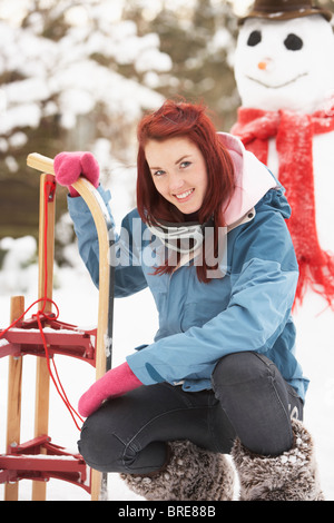 Teenage Girl With Sledge Next To Snowman Stock Photo