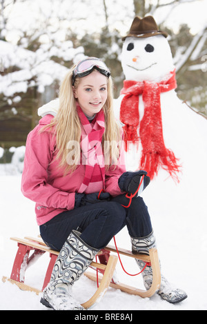 Teenage Girl With Sledge Next To Snowman Stock Photo