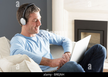 Man Using Laptop Wearing Headphones Relaxing Sitting On Sofa At Home Stock Photo