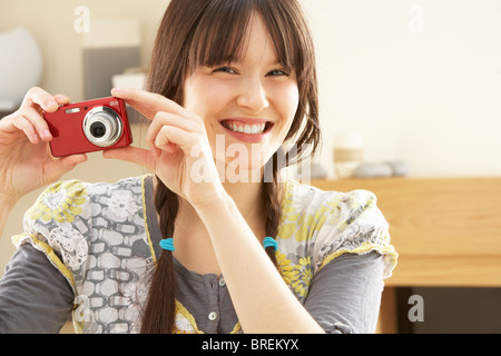 Young Woman Taking Photograph On Digital Camera At Home