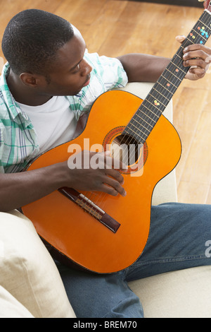 Young Man Relaxing Sitting On Sofa Playing Acoustic Guitar Stock Photo
