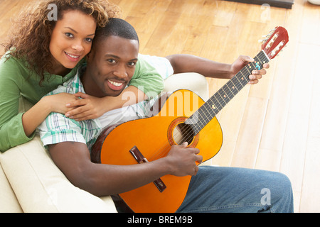 Young Couple Relaxing Sitting On Sofa Playing Acoustic Guitar Stock Photo