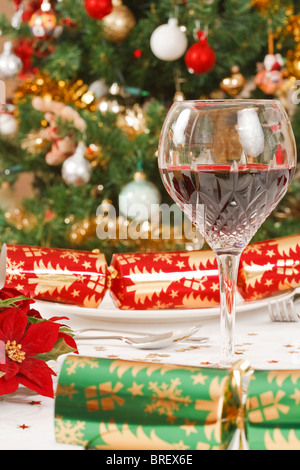 Chistmas crackers, christmas tree and a crystal glass with wine on a dining table Stock Photo