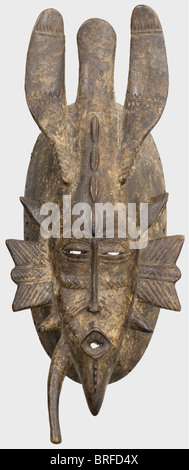 A Kpelie mask of the Senufo people, Ivory Coast, first quarter of the 20th century. Delicately carved wood mask with tri-lobed ornamentation (small break) and characteristic pointed elements attached to the temples and chin (one broken off). Slit-like eyes, oval, strongly protruding mouth, geometrical tribal scars. On the edge circumferential fastening holes for the headdress of natural fibres. Lightly patinated, signs of age and wear. Height 32 cm. The mask comes from the holdings of the Musée d'Art Africain founded by Theodore Monod in Dakar in 1936, which pr, Stock Photo