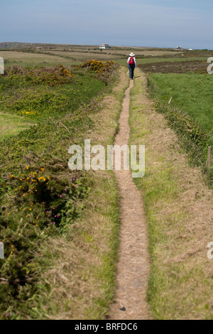 Walking the Lizard paths. A woman with a small red backpack walks along a path embedded into an ancient stone wall. Stock Photo