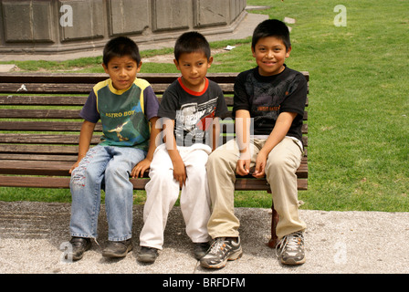 Three Mexican boys sitting on a park bench in Cholula, Puebla, Mexico Stock Photo