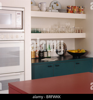 Close-up of microwave and oven in fitted unit beside glasses and crockery on kitchen shelves Stock Photo