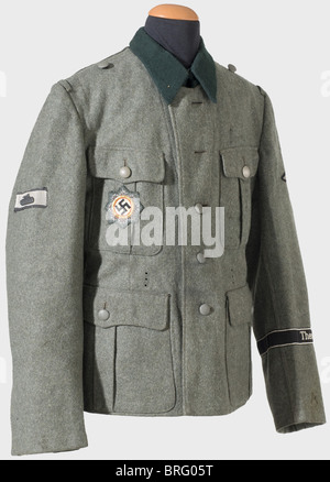 A model 36 tunic,for a member of the 'Theodor Eicke' Regiment. Issue item of field grey,woolen material,the army version with three holes for the belt hooks,dark green collar(moth damage),brown cotton lining stamped with the Munich manufacturer's label and size. Machine-sewn,BeVo version,sleeve eagle. Hand-sewn black sleeve band(BeVo version)with silver grey edging and inscription. Cloth version of the German Cross in Gold on Army fabric. A front-made special badge for tank destruction by an individual soldier(an iron tank silhouette on the back of a,Additional-Rights-Clearences-Not Available Stock Photo