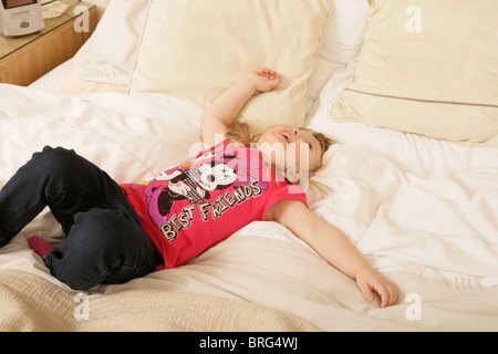 A three year old girl lying on her back in a big bed. Stock Photo