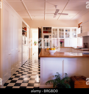 Black+white checkerboard vinyl flooring in large modern white kitchen with wooden worktops on fitted units Stock Photo