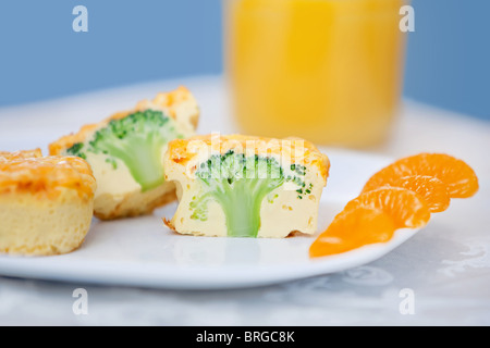 two broccoli cheddar frittata muffins with oranges and orange juice on a white tablecloth Stock Photo