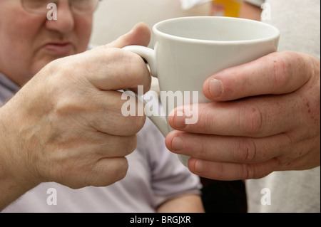 male carer (son) giving a drink to a disabled elderly man Stock Photo