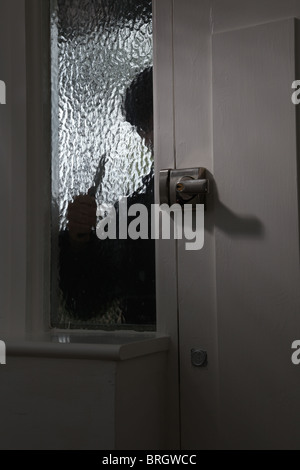 Figure of someone outside looking through an opaque glass window, holding a knife Stock Photo