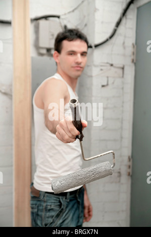attractive young adult man holding a paint roller toward the camera Stock Photo