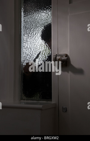 Figure of someone holding a knife outside on opaque glass window by a front door Stock Photo