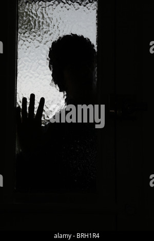 Silhouette male intruder looking through an opaque window next to a front door Stock Photo